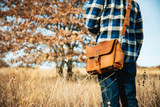 High quality model standing in front of a tree with the rounded leather satchel in tan on. Made by Saddleback