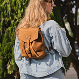 High quality tan leather 10" tumbled drawstring backpack outdoors on a woman model. Made by Saddleback