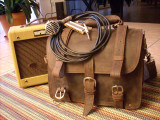 High quality full grain leather briefcase with a harmonica and amp next to it.