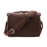 High quality back of a slim red brown leather briefcase with its shoulder strap laying in front of it.