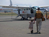 High quality the back picture of the tan brown leather backpack on a woman's back as her toddler son is running towards her in Africa.