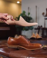 High quality wooden shoe tree held in profile above a brown leather wingtip shoe - Saddleback Leather