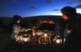 High quality leather travel chess set in the Sahara Desert with a father and son playing with camels waiting behind them.