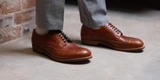 High quality natural tan full grain leather wing tip shoes on foot in side profile against a brick wall - Saddleback Leather