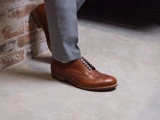 High quality natural tan full grain leather wing tip shoe side profile on foot against a brick wall - Saddleback Leather