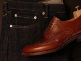 High quality red brown full grain leather wing tip shoe side profile flat lay with dark raw selvedge denim - Saddleback Leather