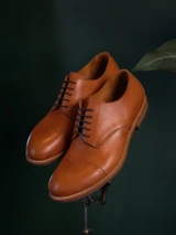 High quality tan full grain leather toe cap shoes elevated studio portrait on stand with dark green background - Saddleback Leather