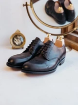 High quality black full grain leather toe cap shoes studio three-quarter front view with wooden shoe trees and vanity mirror - Saddleback Leather