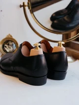 High quality black full grain leather toe cap shoes rear three-quarter view showing heel counters and wooden shoe trees - Saddleback Leather