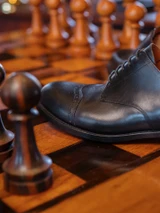 High quality close-up of black full grain leather toe cap shoe brogue perforation detail on chessboard - Saddleback Leather
