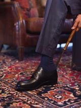 High quality black full grain leather toe cap shoe being put on with wooden shoe horn, side profile on oriental rug - Saddleback Leather