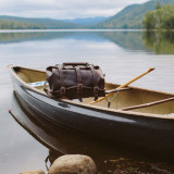 High quality dark brown leather duffle bag with three straps on the front of a canoe on a lake.