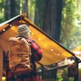 High quality tan brown leather duffle bag that is on a man's back being used as a backpack.