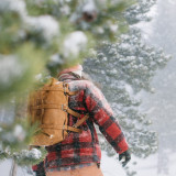 High quality tan brown leather duffle bag with three straps on front to hold overnight travel gear on a man's back in the snow.