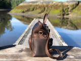High quality this dark brown women's leather backpack is on a dock in Canada near Tofino and is showing the side.