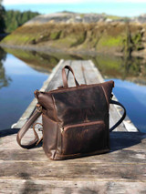 High quality this dark brown women's leather backpack is on a dock in Canada near Tofino and is showing the front angle.