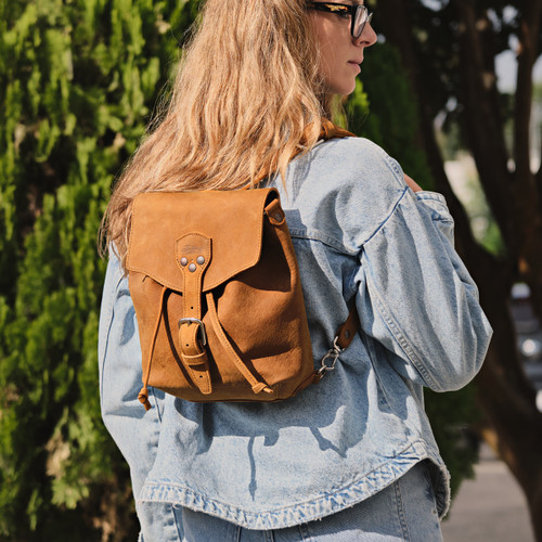 High quality tan leather 10" tumbled drawstring backpack outdoors on a woman model. Made by Saddleback