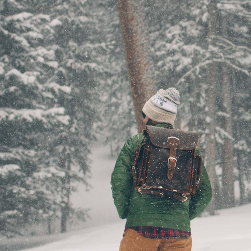 High quality this  is a man lost in the snow wearing a dark brown leather backpack.