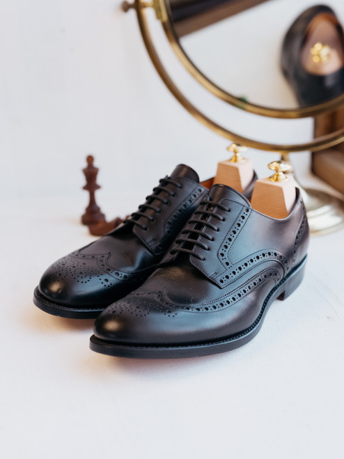 High quality black full grain leather wing tip shoes studio three-quarter front view with wooden shoe trees and brass mirror - Saddleback Leather