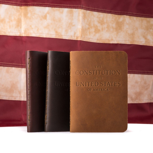 Desk size Constitution of the United States for the pocket. This picture has three in different colors in front of an American flag.