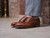High quality natural tan full grain leather wing tip shoes three-quarter on-foot view by a brick wall - Saddleback Leather