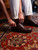 High quality dark oak full grain leather toe cap shoes being pulled on by hand, side view on oriental rug - Saddleback Leather
