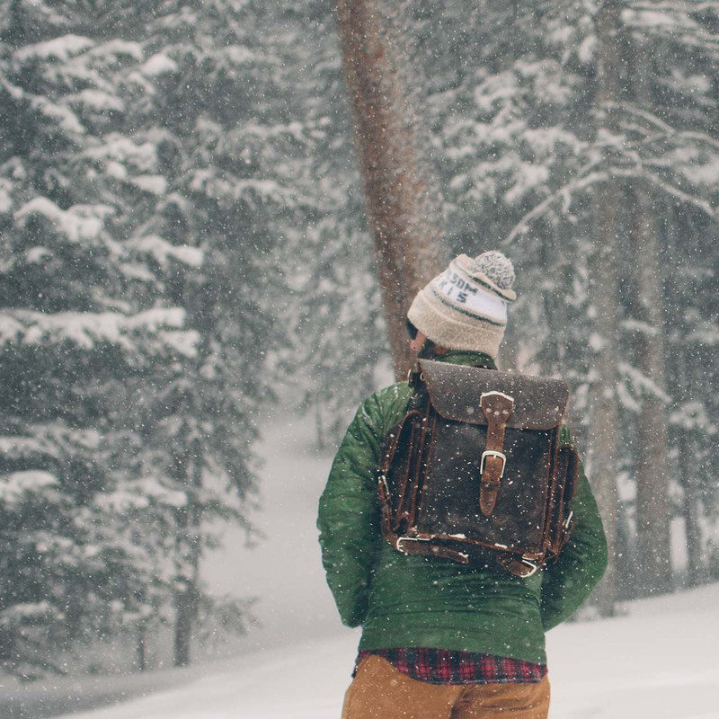High quality this  is a man lost in the snow wearing a dark brown leather backpack.
