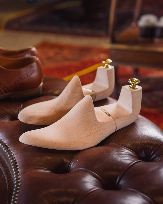 High quality wooden shoe trees resting on a tufted leather ottoman with brown shoe - Saddleback Leather