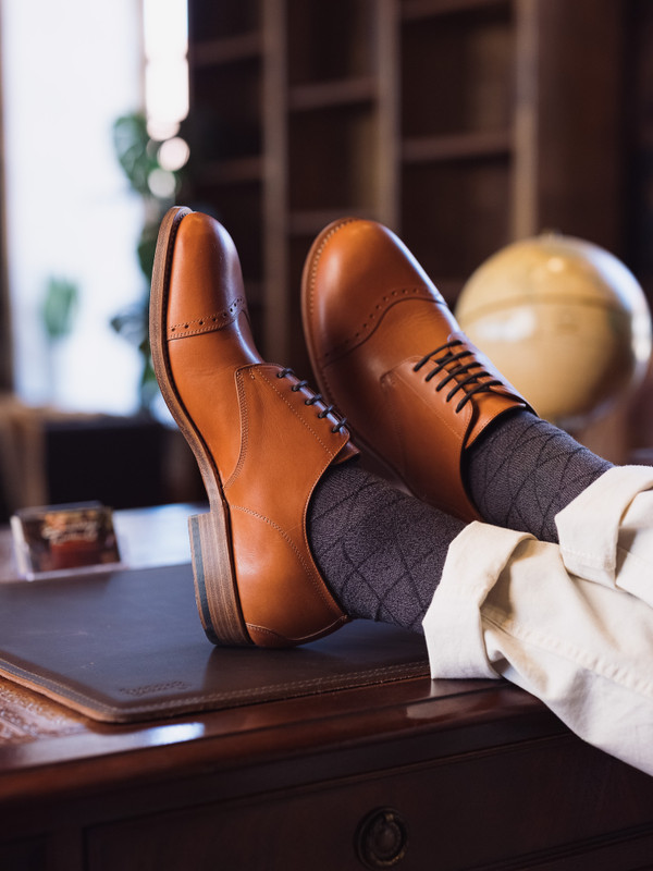 High quality tan full grain leather toe cap shoes lifestyle shot with feet propped on wooden desk - Saddleback Leather