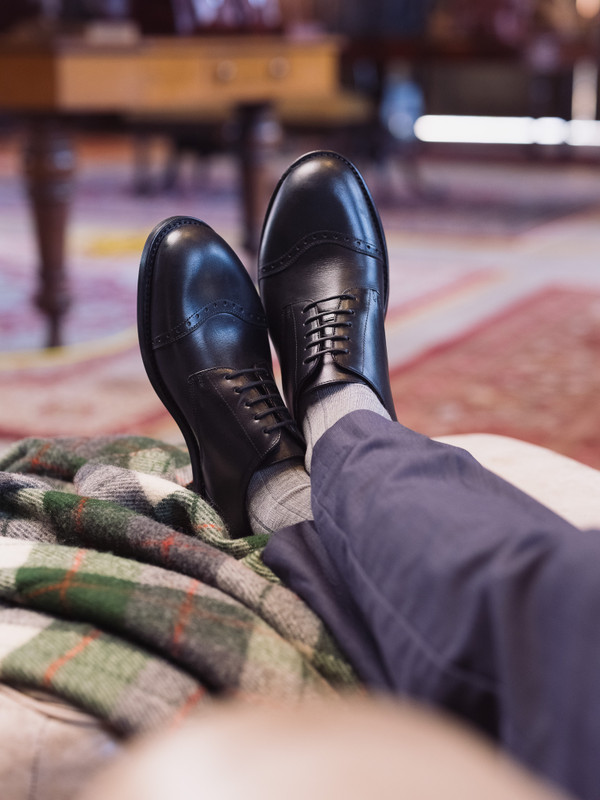 High quality black full grain leather toe cap shoes lifestyle shot on-foot resting on ottoman in study - Saddleback Leather