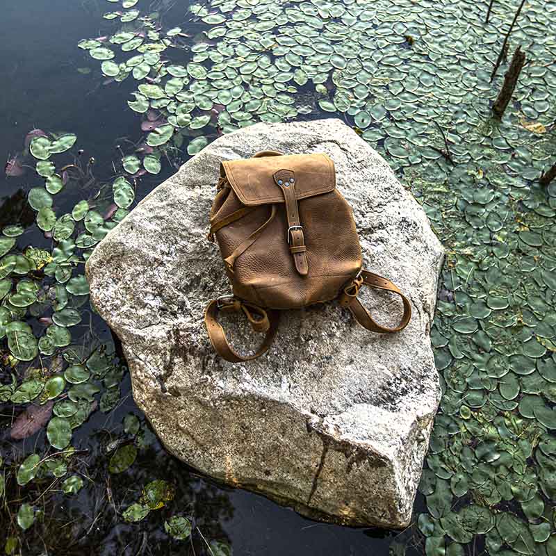 The 12" Full Grain Leather Drawstring Backpack is designed with simplicity and functionality in mind, featuring a wide opening, pigskin-lined back, laptop pocket, and adjustable shoulder straps.