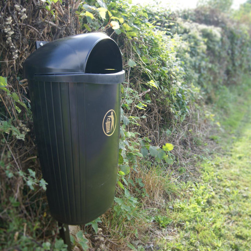 Leafield Regent Hooded Post / Wall Litter Bin 50 Litre, black outdoor waste receptacle mounted on a post beside a hedge and grassy path.