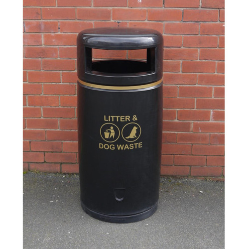 Roadware 90L Coniston Floor Mount Dog Waste Bin, black outdoor trash can with gold text and icons for litter and dog waste against a brick wall.