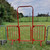 Hermeq 2.3m Spring Gated Site Access Walkthrough Barrier, red metal barrier with gate and archway on green grassy field in outdoor setting.