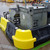 Oaklands Corner Section For EVO 1 & 1.5 Metre Barrier, yellow and black corner barrier surrounding a metal container on a wet industrial surface.