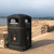 Leafield 240 Litre XL Square Heritage Outdoor Litter Bin, black outdoor litter bin with two compartments, situated on a seaside promenade with sandy beach and distant horizon in the background.