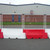 Oaklands Mesh Top Panel For Novus Water Filled Barrier, white and red plastic barriers in front of a metal fence and building.