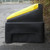 Excelsior 200 Litre Heavy Duty Grit Bin Kit With 200kg Rock Salt, black and yellow durable grit bin placed on asphalt outside near some bushes.