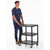GPC Multi-Purpose 3 Shelf Service Table Trolley, black metal frame with three flat shelves on wheels being pushed by a man in casual clothing.