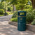 Roadware Grasmere 120 Litre Outdoor Heritage Litter Bin, dark green outdoor bin with gold trim and litter symbol beside a paved garden path