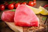 Yellowfin tuna steaks on a wood board with tomatoes and lemons