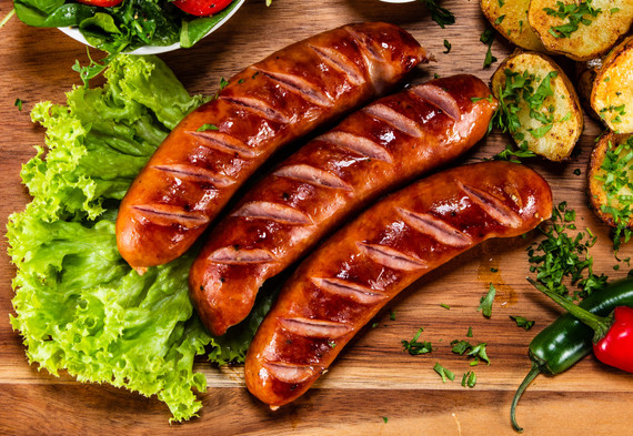 Albert's Knockwurst displayed on wooden board surrounded by lettuce and peppers.