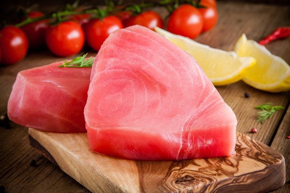 Yellowfin tuna steaks on a wood board with tomatoes and lemons
