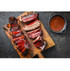 Sliced Beef Back Ribs on a wooden cutting board next to a bowl of sauce