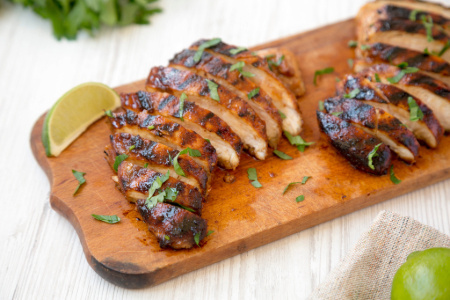 Grilled chipotle chicken breast on a wooden board with a lime slice and garnish