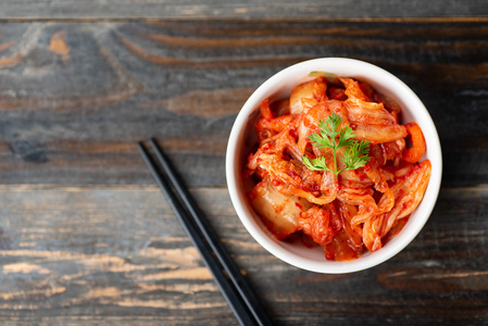 Koren Bowl of Kimchi on a wood grain table next to chopsticks