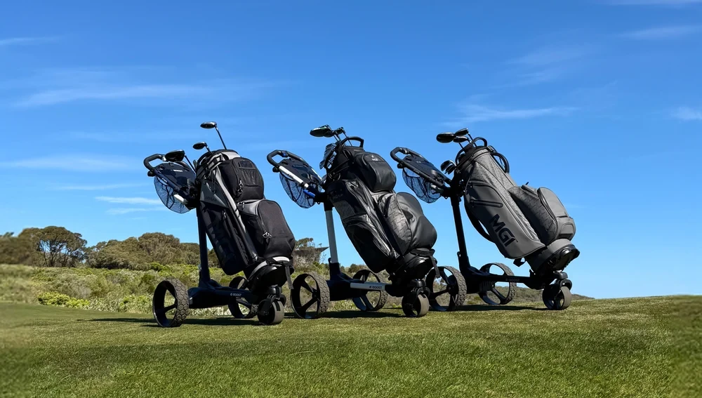 Three MGI pushcarts with golf bags lined up on the course