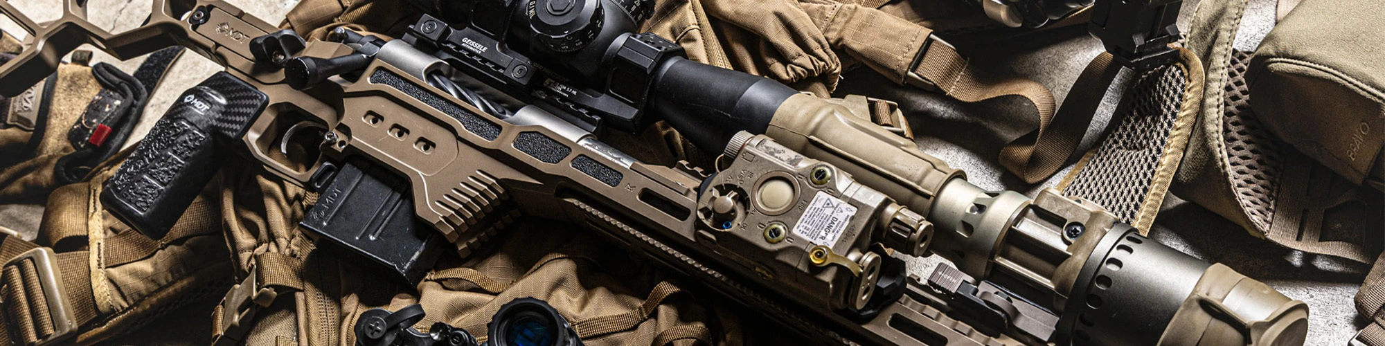 MDT DRT Chassis System rifle in FDE with a clip-on thermal, laid out with night vision goggles and a helmet on a pack