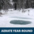 A snow-covered, frozen pond with a large ice hole around aeration bubbles, with text: “Aerate year-round”. View Product Image