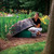 A woman lifts the DekoRRa Model 111 rock enclosure, revealing a green utility cover. The lightweight, durable rock blends into the landscape. View Product Image
